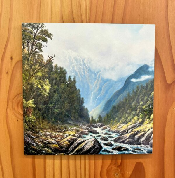 The "A Walk in the Wilderness Wall Tile" features a scene of a mountainous landscape with a flowing river, framed by lush green trees and misty peaks in the background, perfect for mounting on a wooden wall.