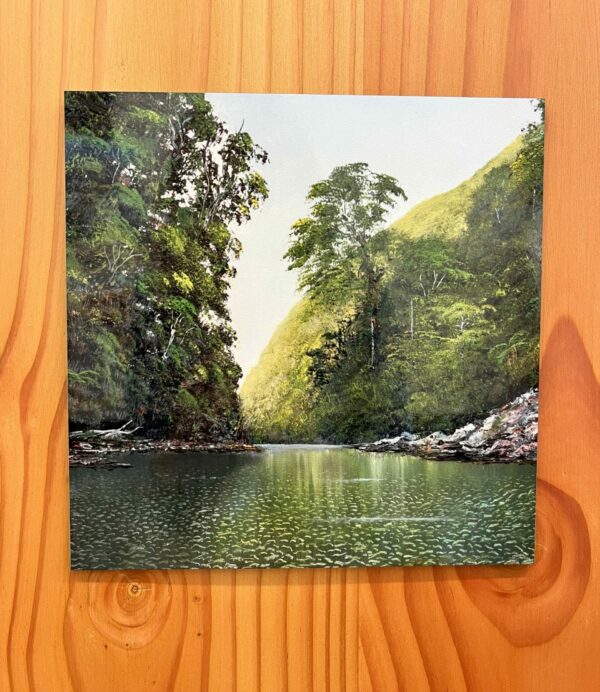 A serene depiction of a river scene with lush green trees on both sides, calm water reflecting the landscape, set against a wooden background is beautifully captured in the Shallow Waters Wall Tile.