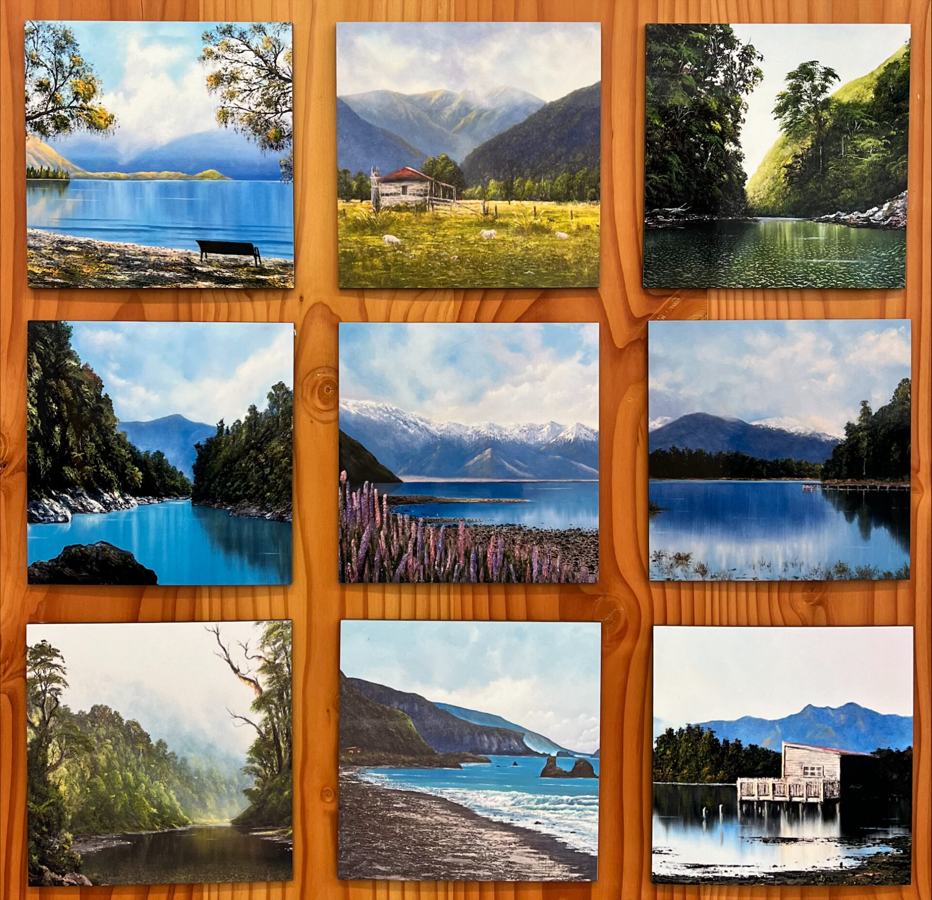 A grid of nine landscape paintings depicting lakes, mountains, trees, and coastal scenes on a wooden background.