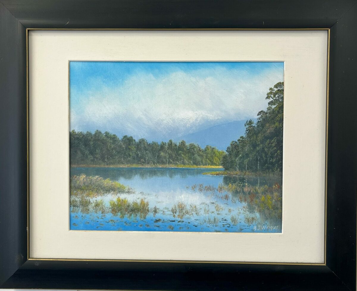 Framed landscape painting titled "Lake Mahinipua," depicting a lake encircled by trees beneath a clear blue sky.