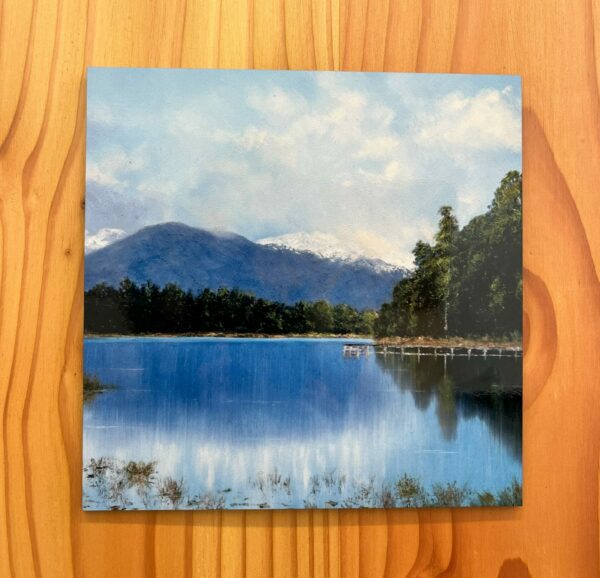 A depiction of Lake Mahinipua, featuring a serene lake with a wooden dock, lush trees, and mountains under a partly cloudy sky, is captured on this wall tile.