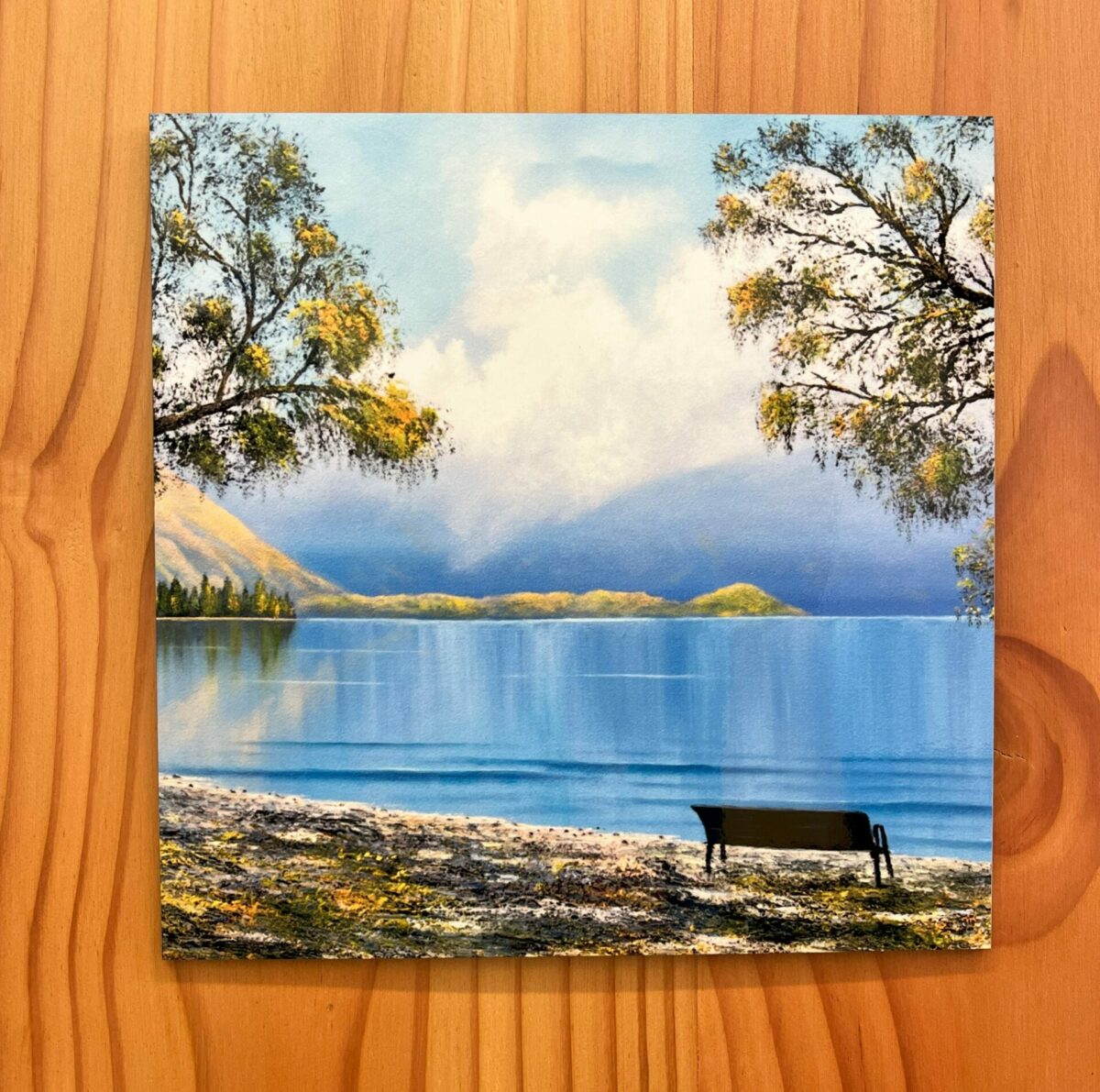 Lake Wanaka Wall tile featuring a serene lakeside scene with a bench, surrounded by trees and set against a mountain backdrop.