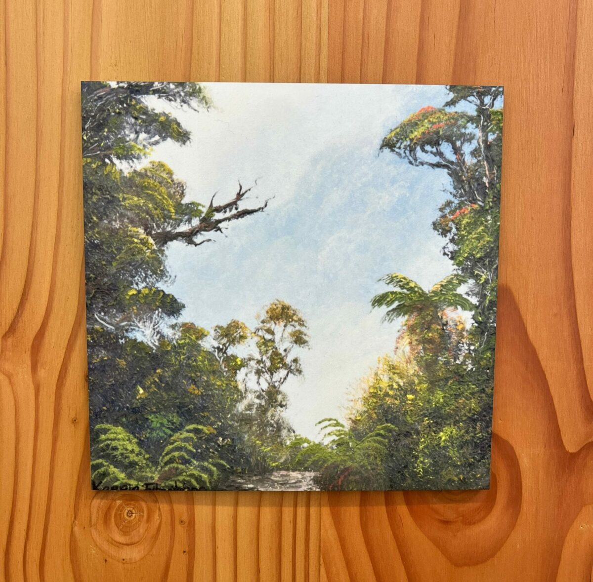 A South Westland Wall Tile depicting a forest scene with tall trees and a path under a blue sky, mounted on a wooden wall.